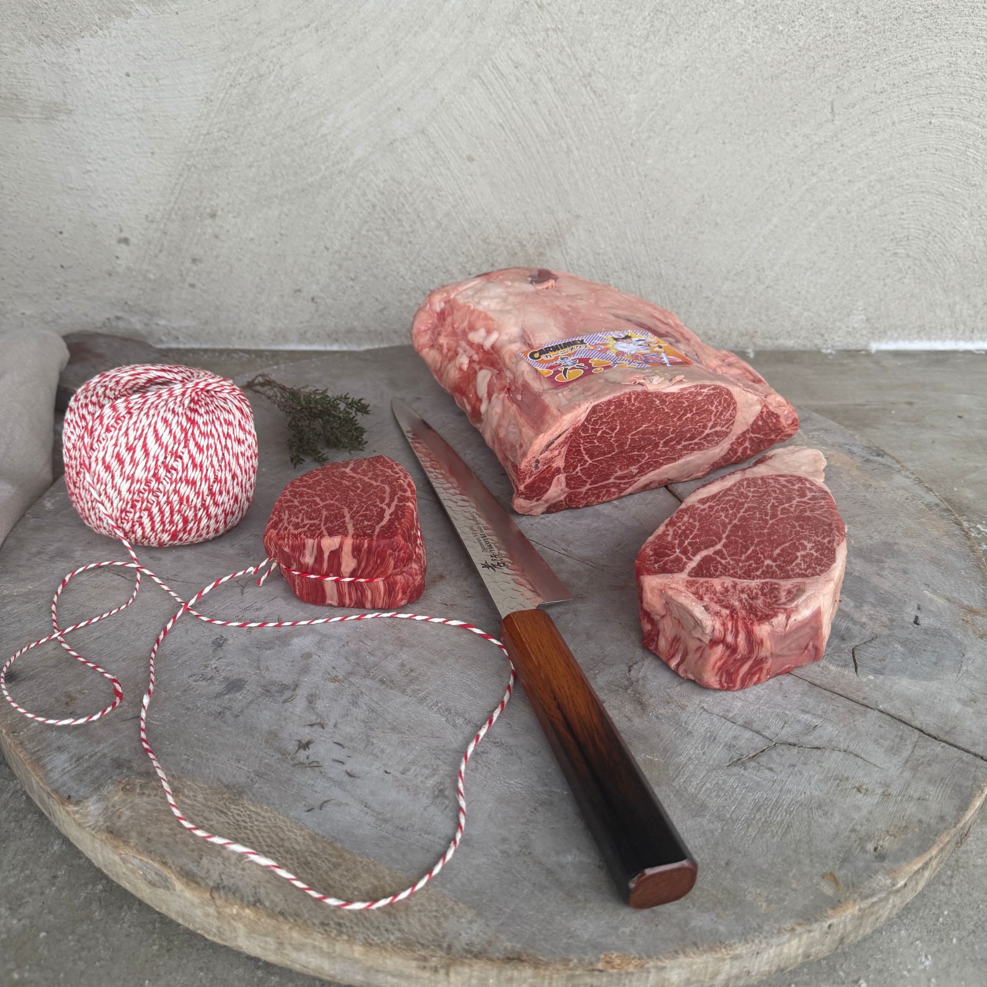 Een hele opgebonden ossenhaas op een rooster met een kernthermometer erin, naast een hete gietijzeren pan met boter, tijm en knoflook klaar om kort af te bakken.